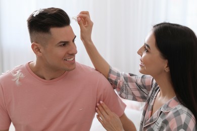 Photo of Happy woman taking off feather from boyfriend's head after pillow fight indoors