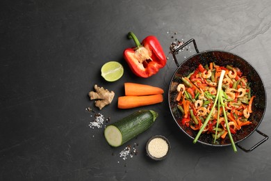 Photo of Shrimp stir fry with vegetables in wok and ingredients on black table, flat lay. Space for text