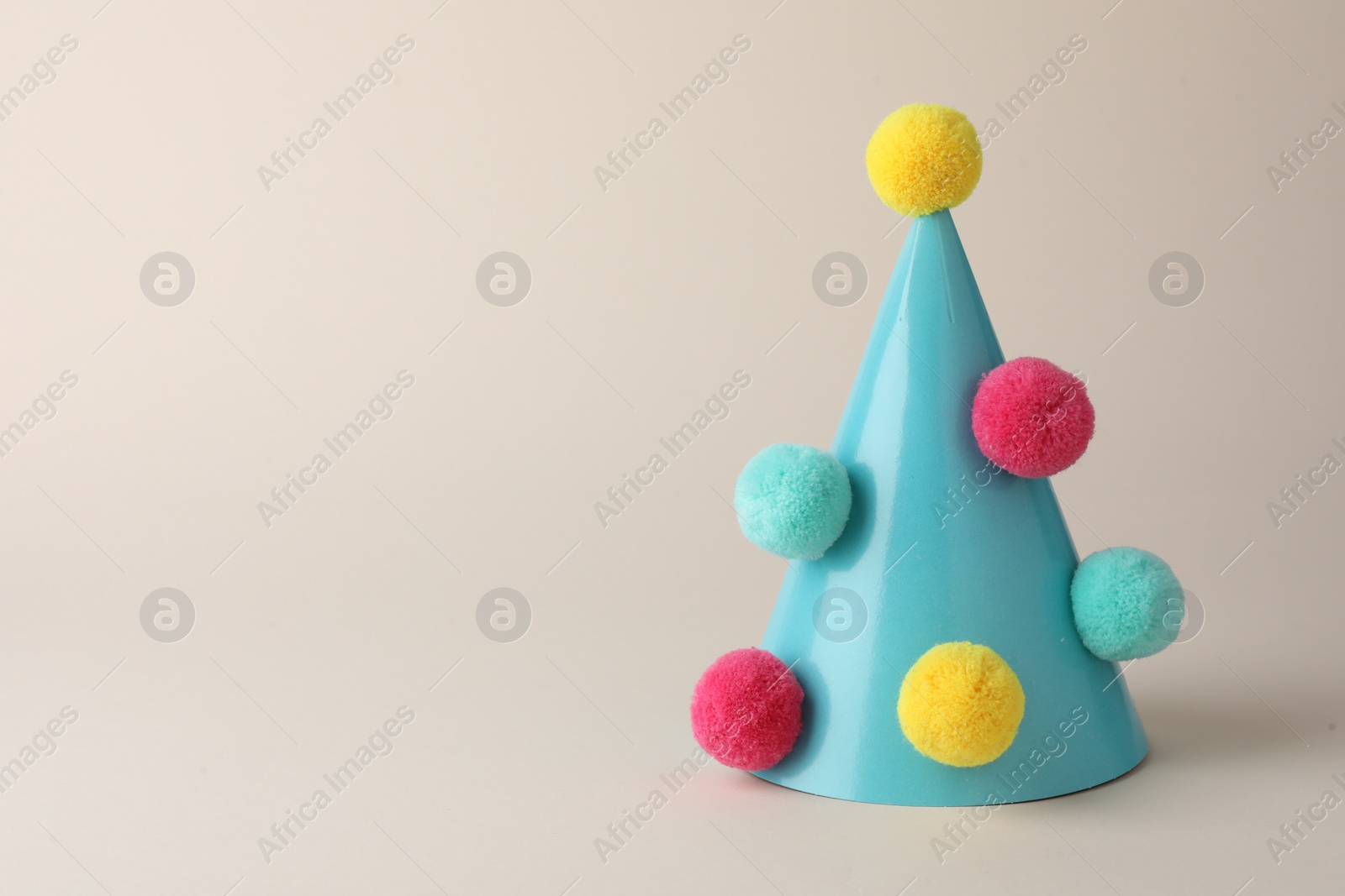 Photo of One light blue party hat with pompoms on beige background. Space for text