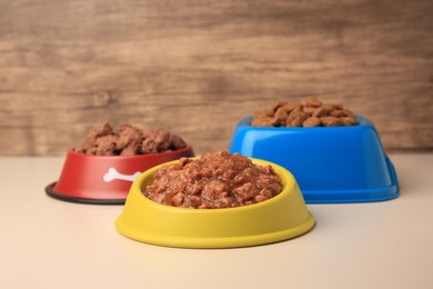 Photo of Dry and wet pet food in feeding bowls on beige background