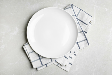 Photo of Empty white plate and napkin on light grey marble table, flat lay