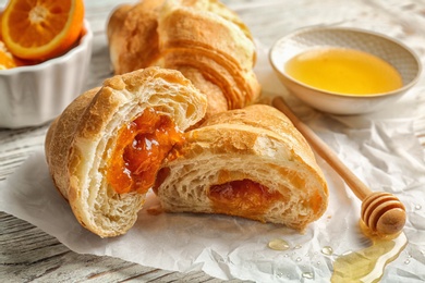 Photo of Tasty croissant with jam and honey on table, closeup