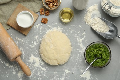 Photo of Making delicious pesto bread. Raw dough and ingredients on grey table, flat lay