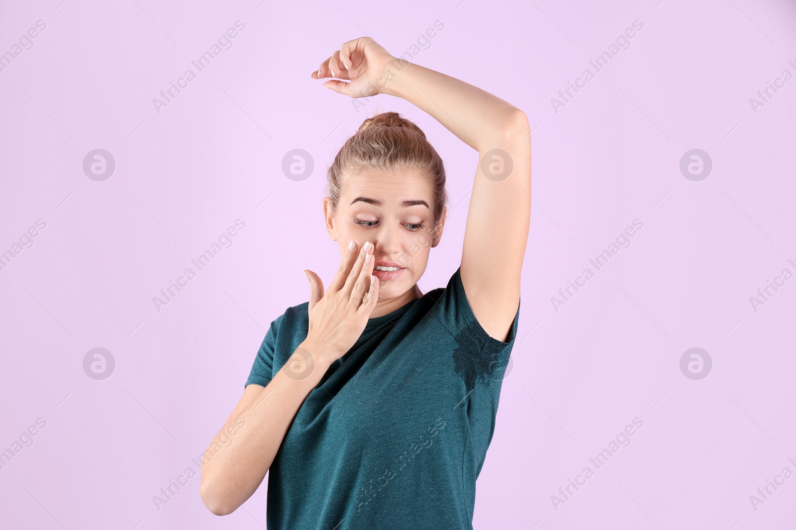 Photo of Young woman with sweat stain on her clothes against color background. Using deodorant