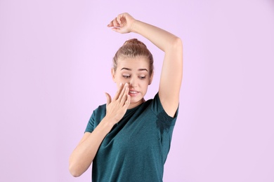 Photo of Young woman with sweat stain on her clothes against color background. Using deodorant