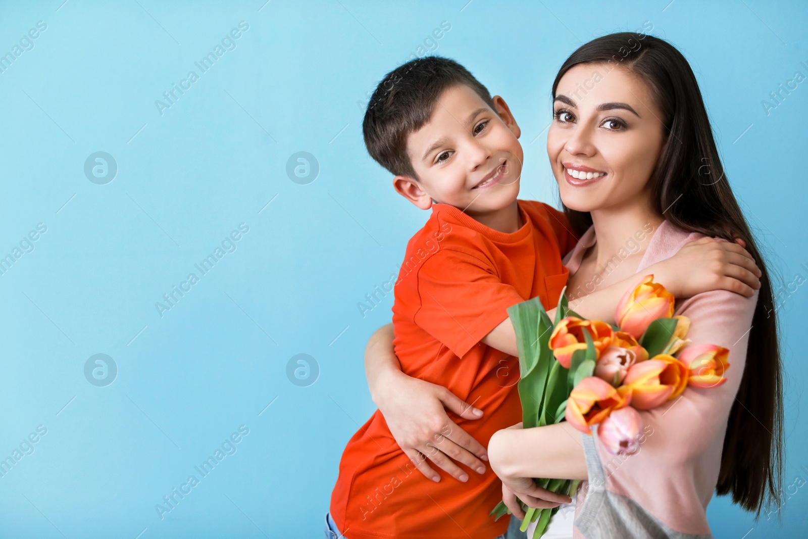 Photo of Portrait of happy woman with flowers and her son on color background. Mother's day celebration