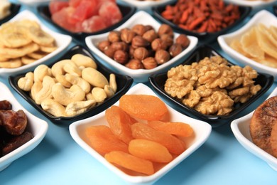 Bowls with dried fruits and nuts on light blue background, closeup