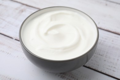 Photo of Delicious natural yogurt in bowl on light wooden table, closeup