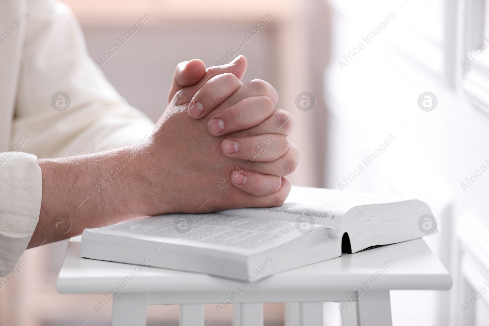 Photo of Religion. Christian man praying over Bible indoors, closeup