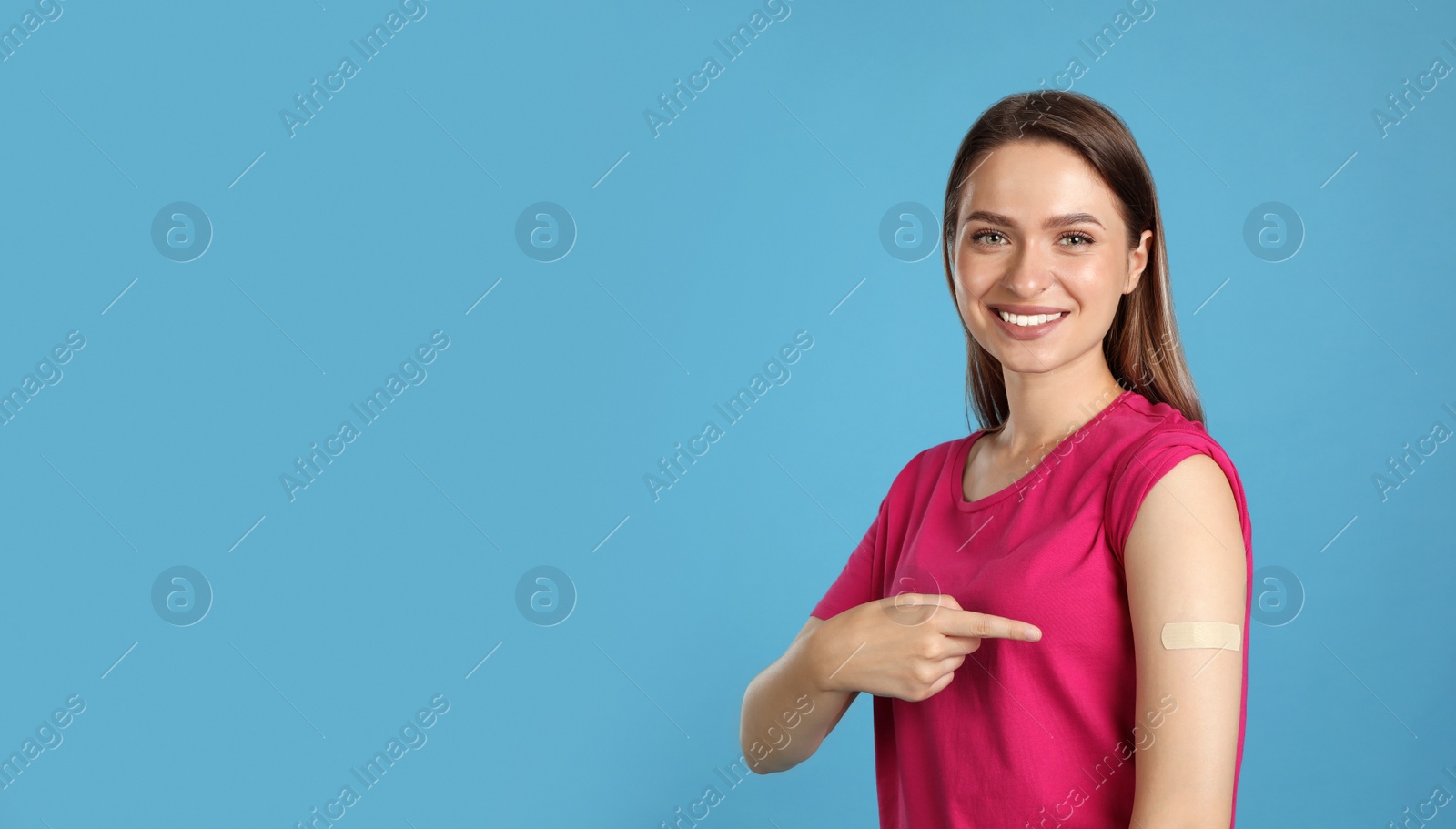 Photo of Vaccinated woman showing medical plaster on her arm against light blue background