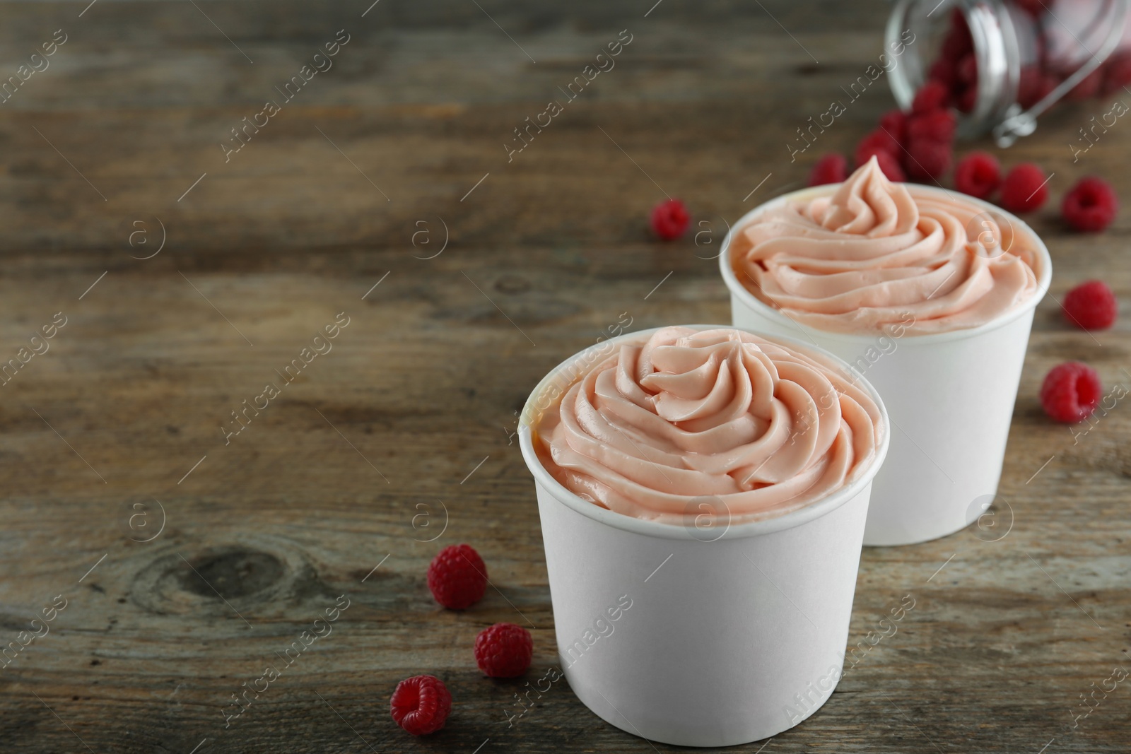 Photo of Cups with tasty frozen yogurt and raspberries on wooden table. Space for text