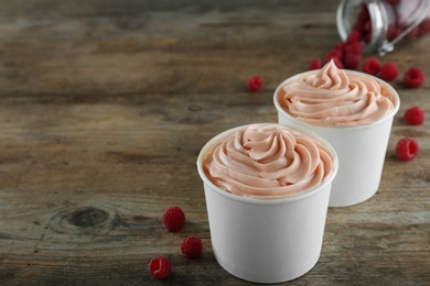 Cups with tasty frozen yogurt and raspberries on wooden table. Space for text