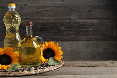 Photo of Sunflower cooking oil, seeds and yellow flowers on wooden table, space for text