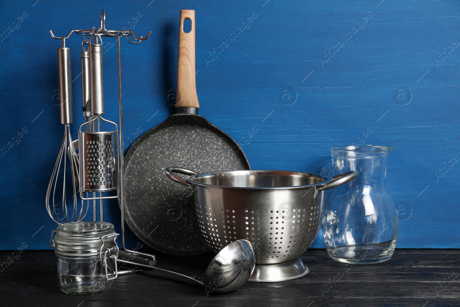 Photo of Set of different kitchen utensils on black table against blue wooden background