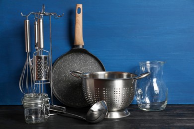 Photo of Set of different kitchen utensils on black table against blue wooden background