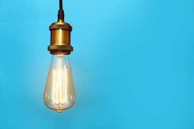 Photo of Pendant lamp with light bulb on color background, space for text