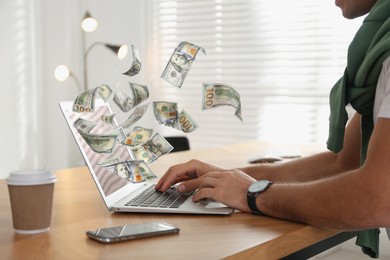 Image of Making money online. Closeup view of man using laptop at table and flying dollars