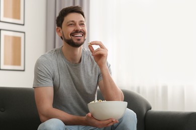 Photo of Happy man with bowl of popcorn watching movie via TV on sofa at home