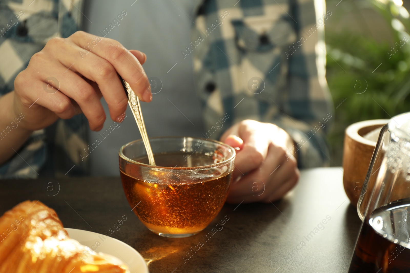 Photo of Woman stirring tea with spoon at dark table, closeup