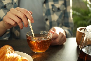 Woman stirring tea with spoon at dark table, closeup