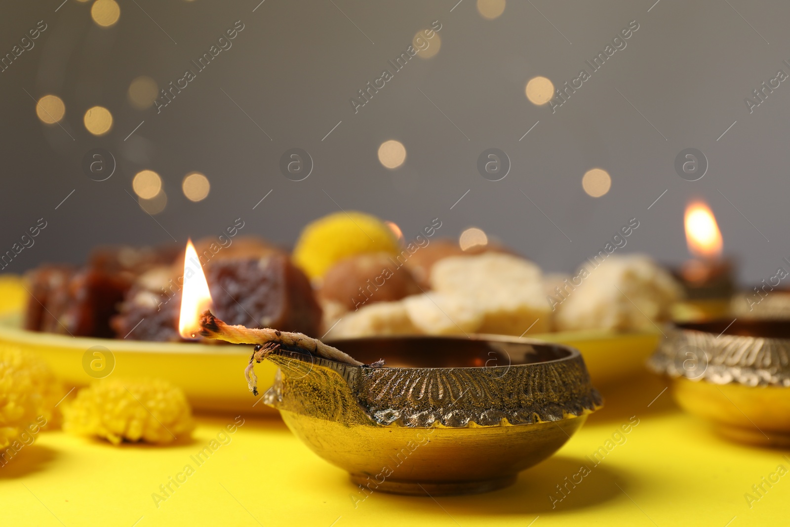 Photo of Happy Diwali. Diya lamp on yellow table against blurred lights, closeup