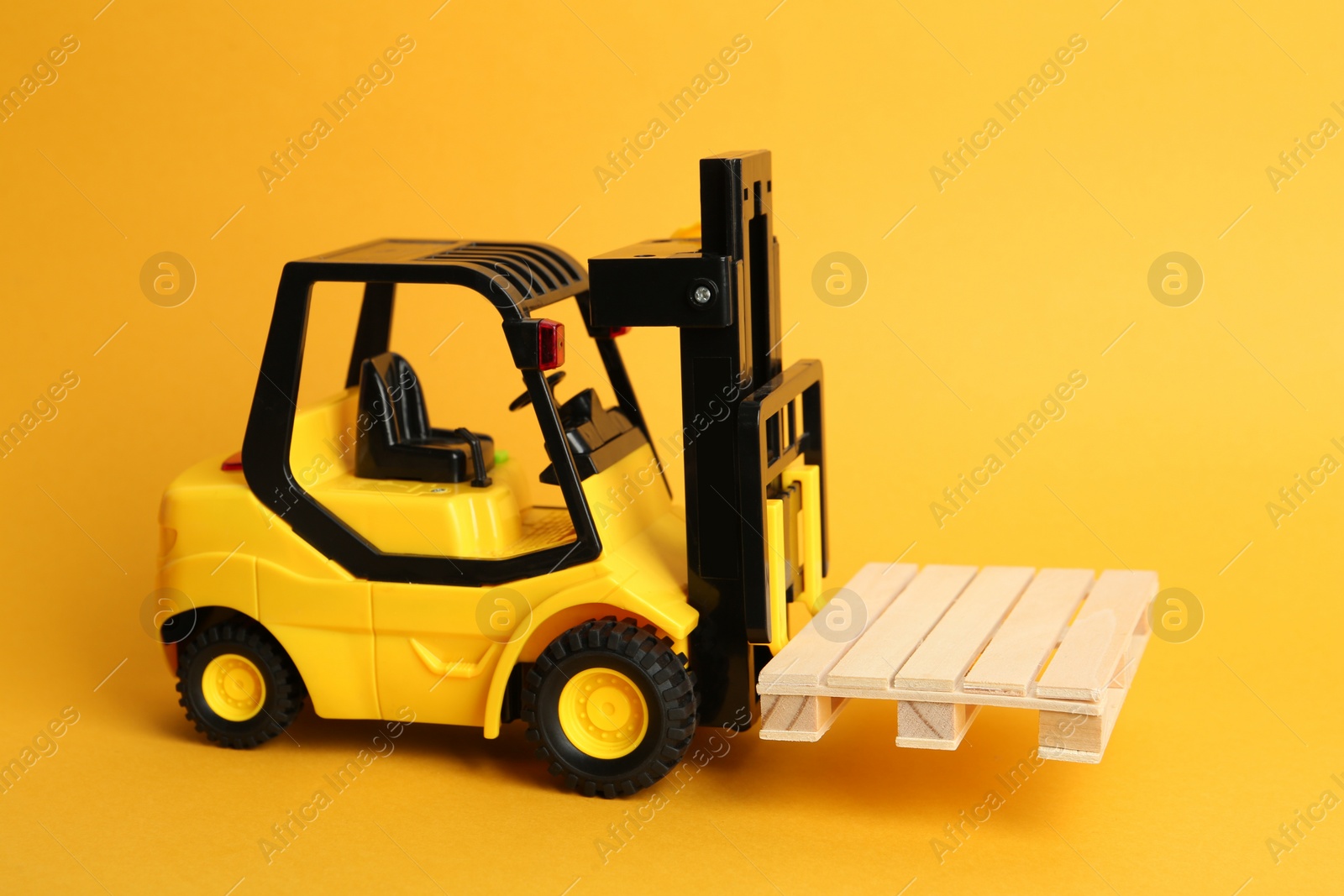 Photo of Toy forklift with wooden pallet on orange background