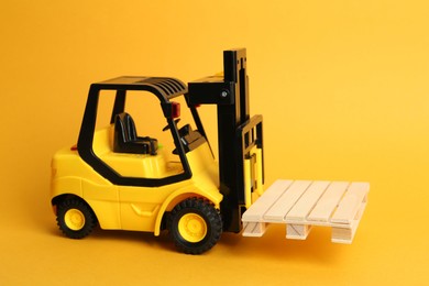 Toy forklift with wooden pallet on orange background