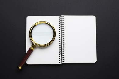 Magnifying glass and notebook on dark background, top view