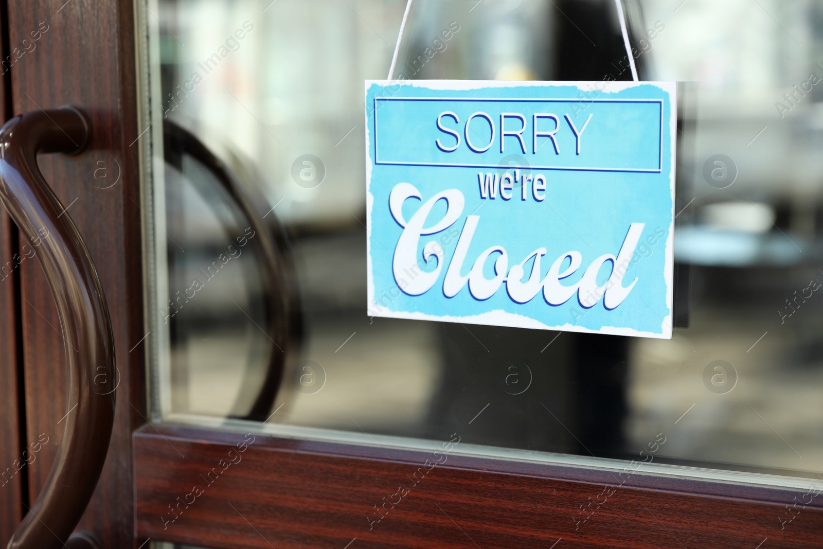 Photo of Light blue sign with text Sorry we're Closed hanging on glass door. Coronavirus quarantine