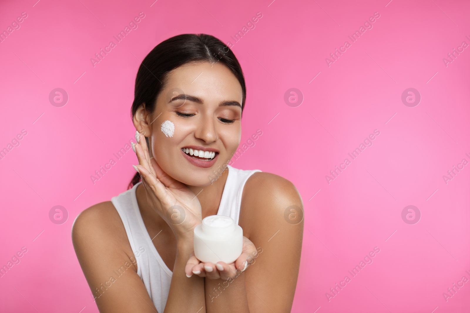 Photo of Young woman applying facial cream on pink background