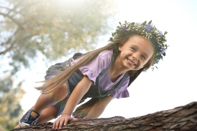 Cute little girl wearing flower wreath on tree outdoors. Child spending time in nature