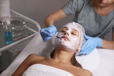 Cosmetologist applying mask on client's face in spa salon