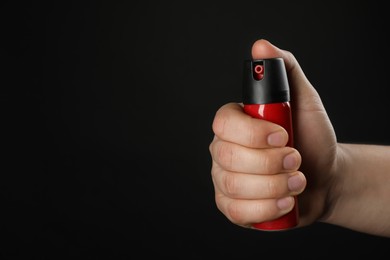 Photo of Man holding pepper spray on black background, closeup. Space for text