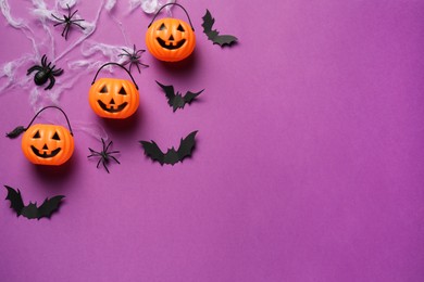 Photo of Flat lay composition with plastic pumpkin baskets, paper bats and spiders on purple background, space for text. Halloween celebration