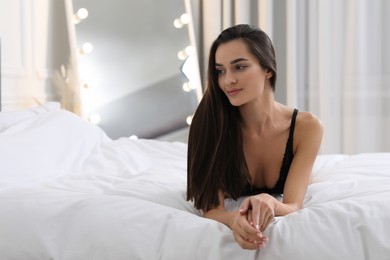 Young woman in elegant black underwear lying on bed indoors. Space for text