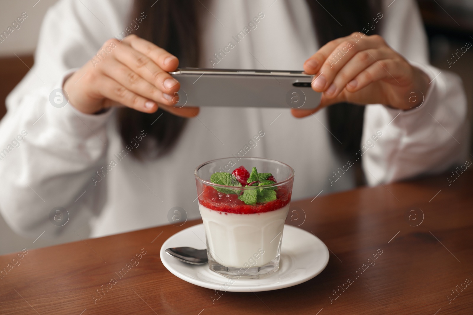 Photo of Young blogger taking picture of dessert at table in cafe, closeup