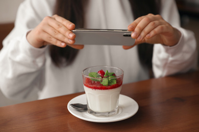 Young blogger taking picture of dessert at table in cafe, closeup