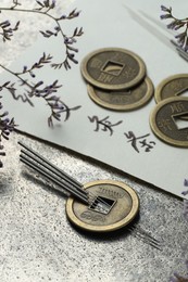 Photo of Acupuncture needles, Chinese coins, flowers and paper with characters on grey textured table