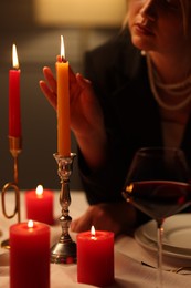 Beautiful young woman near burning candle at table in restaurant, closeup
