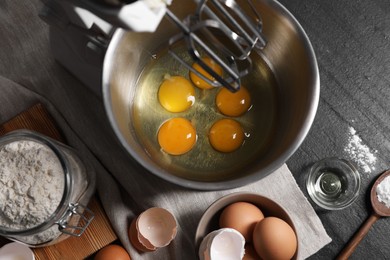 Making dough. Raw eggs in bowl of stand mixer and ingredients on black table, flat lay