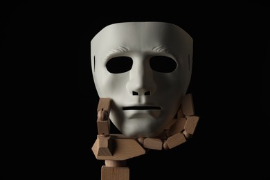 Photo of Wooden mannequin hand holding plastic mask on black background. Theatrical performance