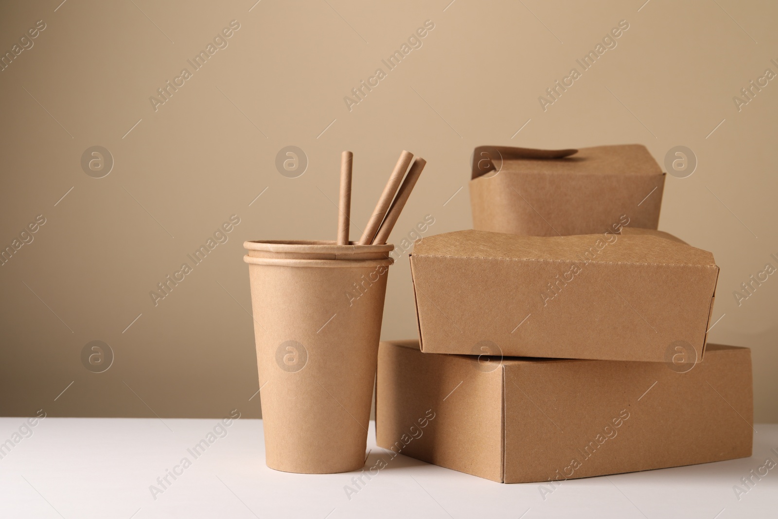 Photo of Eco friendly food packaging. Paper containers and straws on white table against beige background, space for text