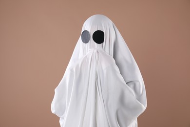 Photo of Creepy ghost. Person covered with white sheet on dark beige background