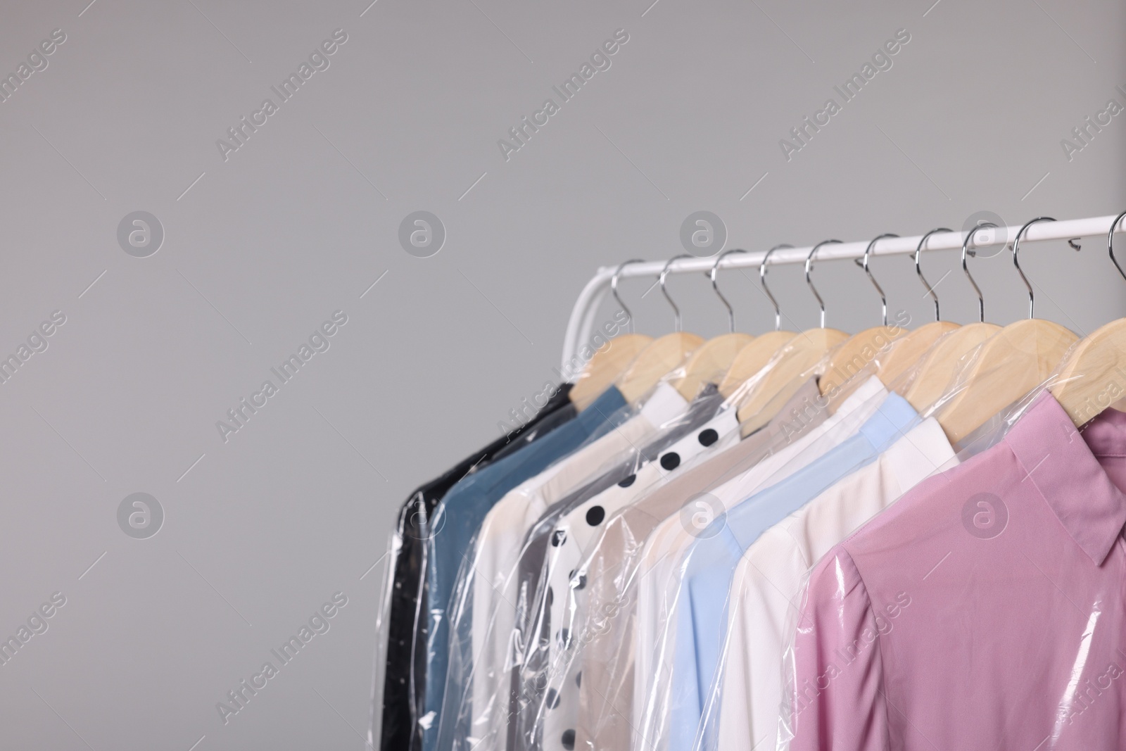 Photo of Dry-cleaning service. Many different clothes in plastic bags hanging on rack against grey background, space for text