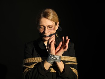 Photo of Woman with bruises tied up and taken hostage on dark background