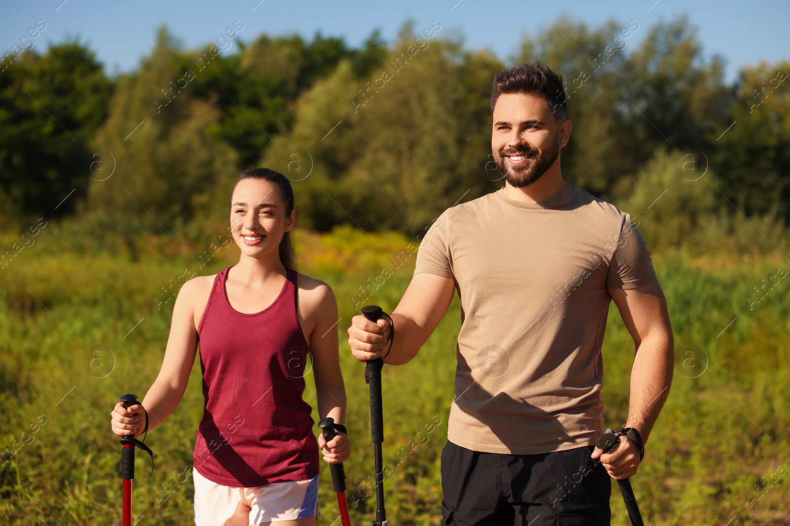 Photo of Happy couple practicing Nordic walking with poles outdoors on sunny day