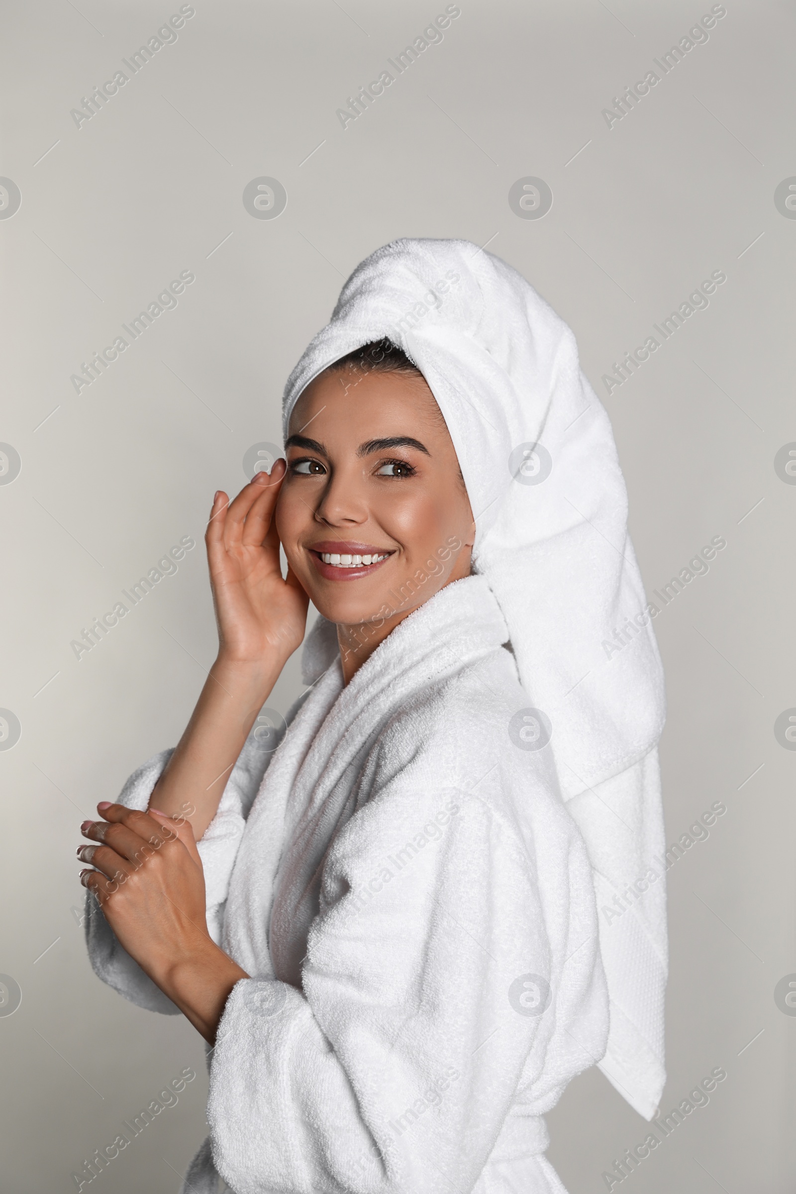 Photo of Beautiful young woman wearing bathrobe and towel on head against light background