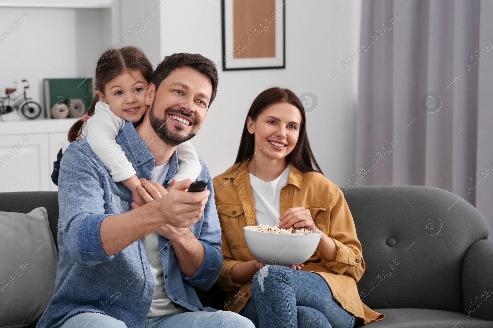 Photo of Happy family watching movie at home. Father changing TV channels with remote control