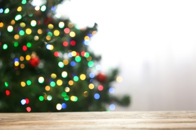 Photo of Blurred view of fir tree with glowing Christmas lights near table indoors. Festive mood