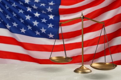 Photo of Scales of justice on light grey table against American flag. Space for text